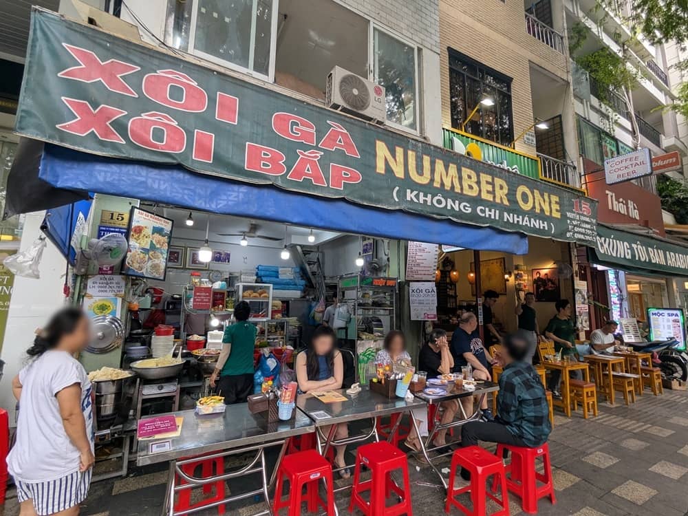 ベトナム・ホーチミン1区にあるソイガーナンバーワン(Xôi Gà Number One)の店舗外観。路上に並んだ赤い椅子と食事を楽しむ人々の様子。