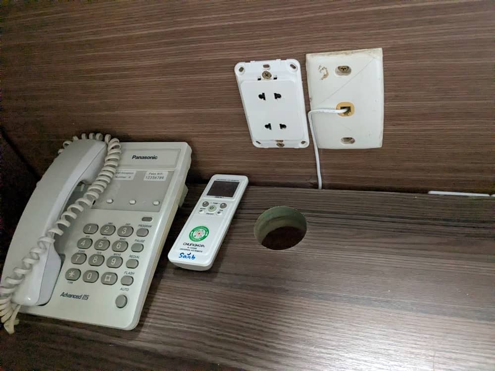 ベッドわきのテーブルにはコンセントと、電話機、クーラーのリモコンがある。