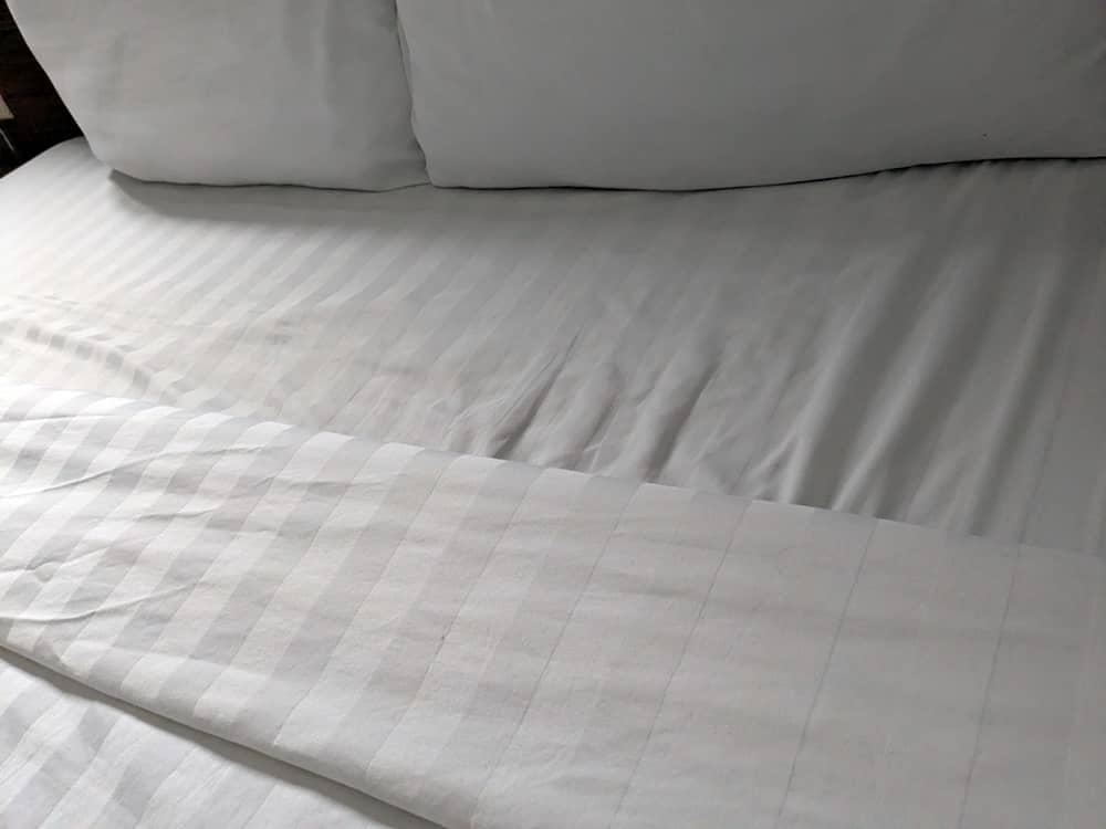 縦ストライプの白いシーツ。清潔感は良好なのが伺える。