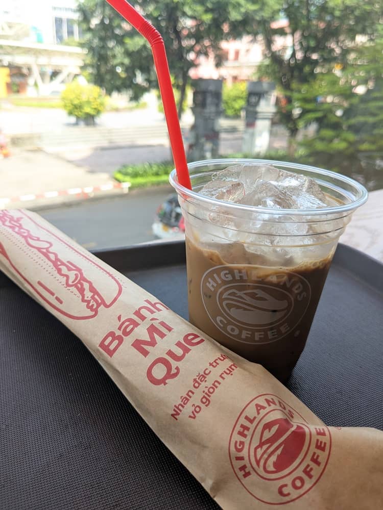 ホーチミン1区のハイランズコーヒー(Highlands Coffee)のベトナムコーヒーとバインミー。窓の外には9月23日公園の緑が広がる風景。