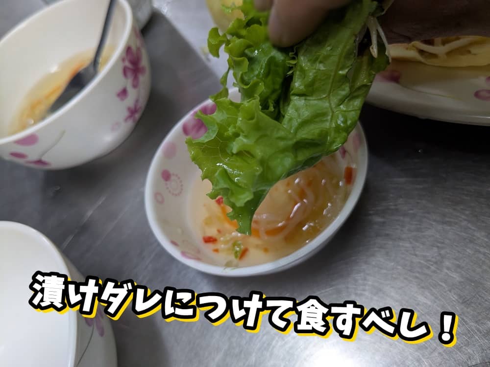 葉物で巻いたバインセオをヌクマムにつける様子。